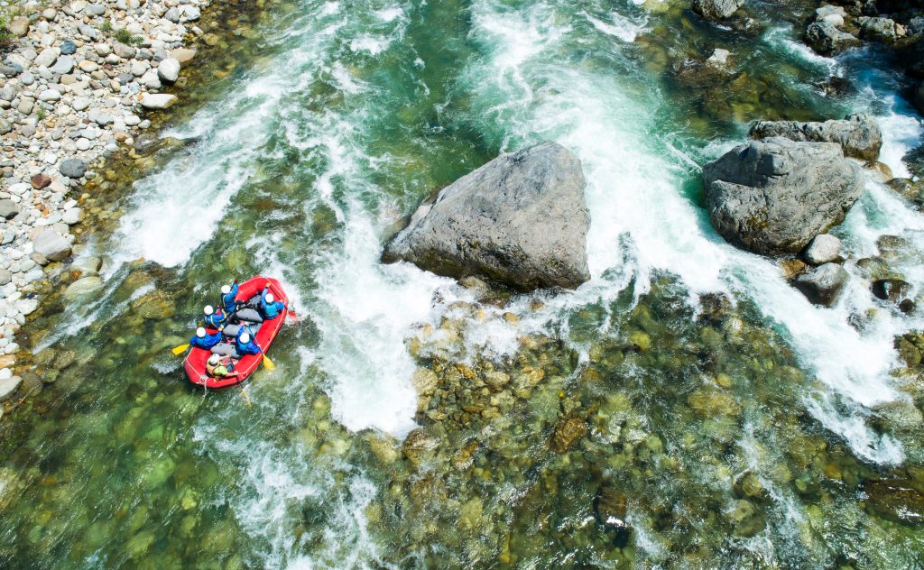 An aerial view of a group of rafters floating down a whitewater section of a river in a red raft.